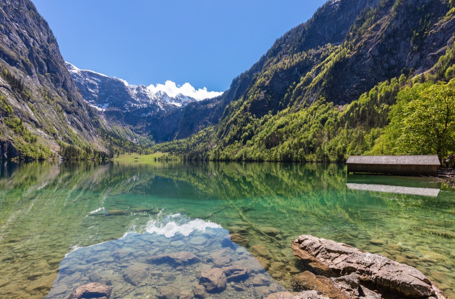 Der Obersee beim Königssee mit klarem, grünem Wasser, einem hölzernen Bootshaus und steilen Bergwänden